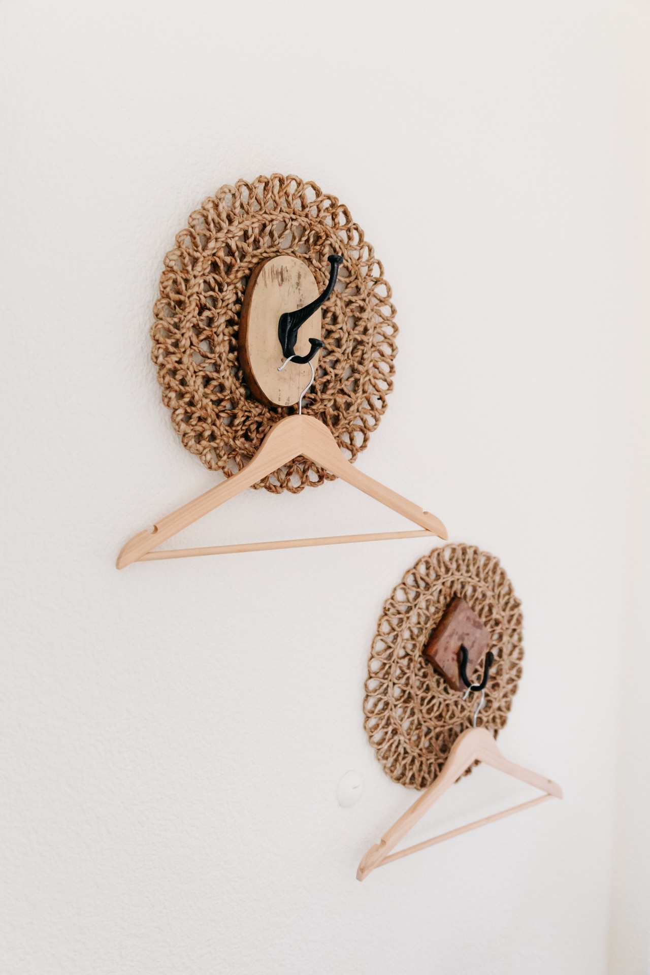 Häkelte runde Wandtasche aus Naturgarn mit Holzkleiderbügeln und schwarzen Haken, vor weißer Wand.